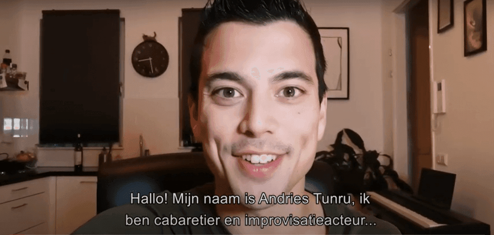 Andries Tunru aan het praten in woonkamer met tekst 'Hallo! mijn naam is andries tunru ik ben cabaretier en improvisatieactuer'