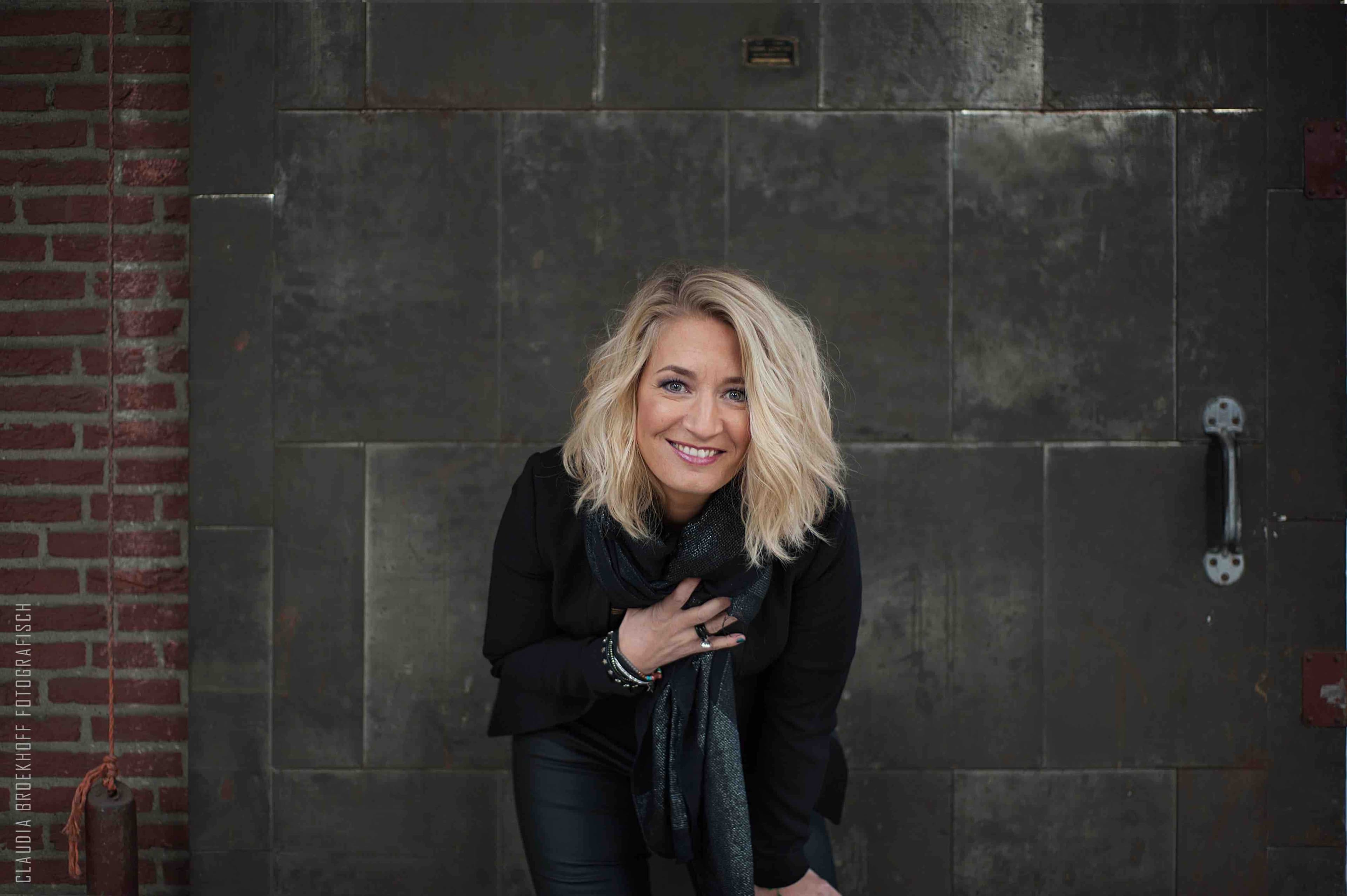 Janneke Jager lachend naar voren gebukt met stenen achtergrond