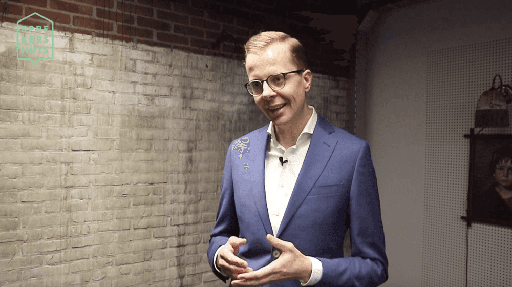Jeroen Baardemans aan het praten bewegend met handen in blauw pak