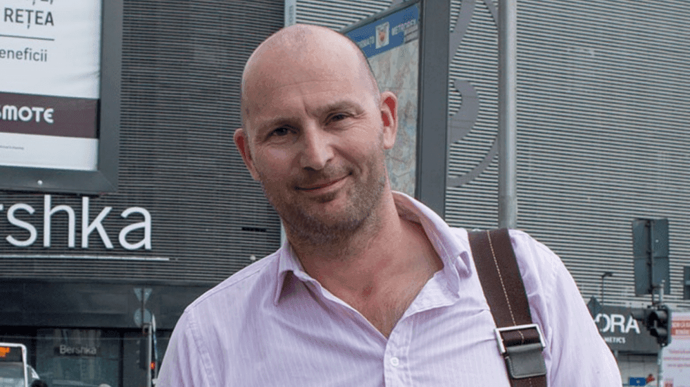 Mark glimlacht naar camera. Hij staat voor Bershka en heeft een tas om zijn schouder hangen