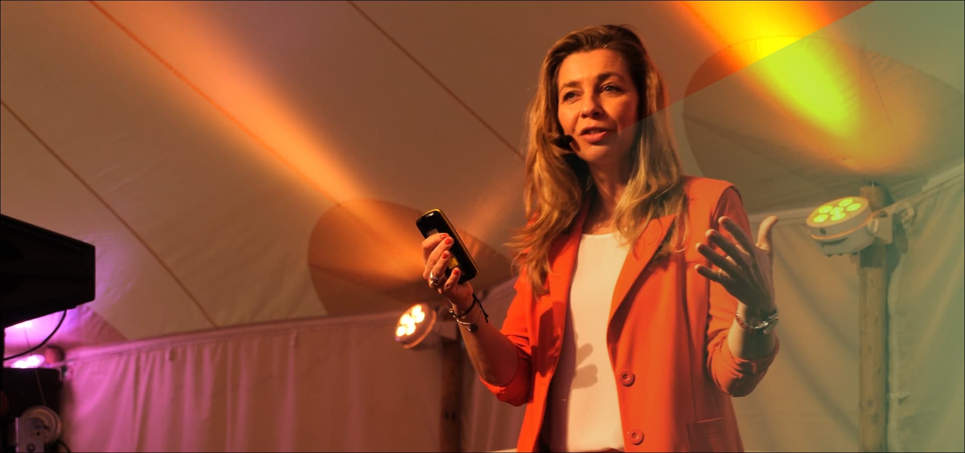 Pauline aan het praten bewegend met handen in rode blazer met oranje licht op achtergrond