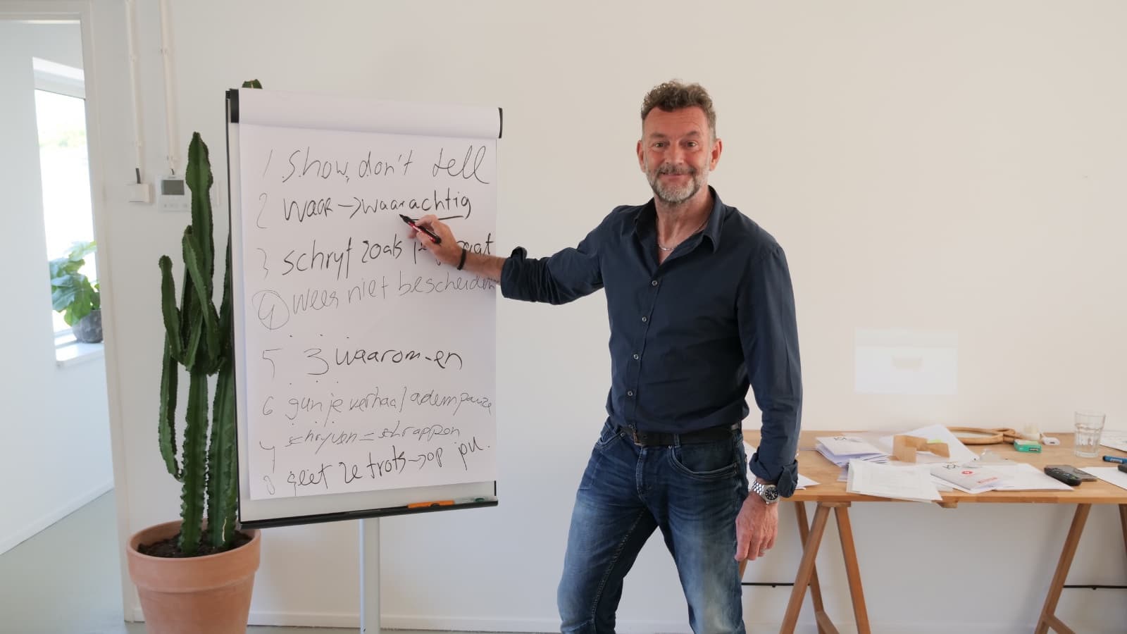 Raymond van de Klundert (Kluun) poserend met hand bij witte schrijfbord onderschreven