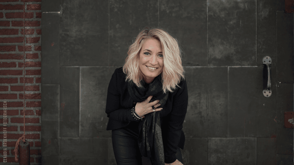 Janneke Jager lachend naar voren gebukt met stenen achtergrond