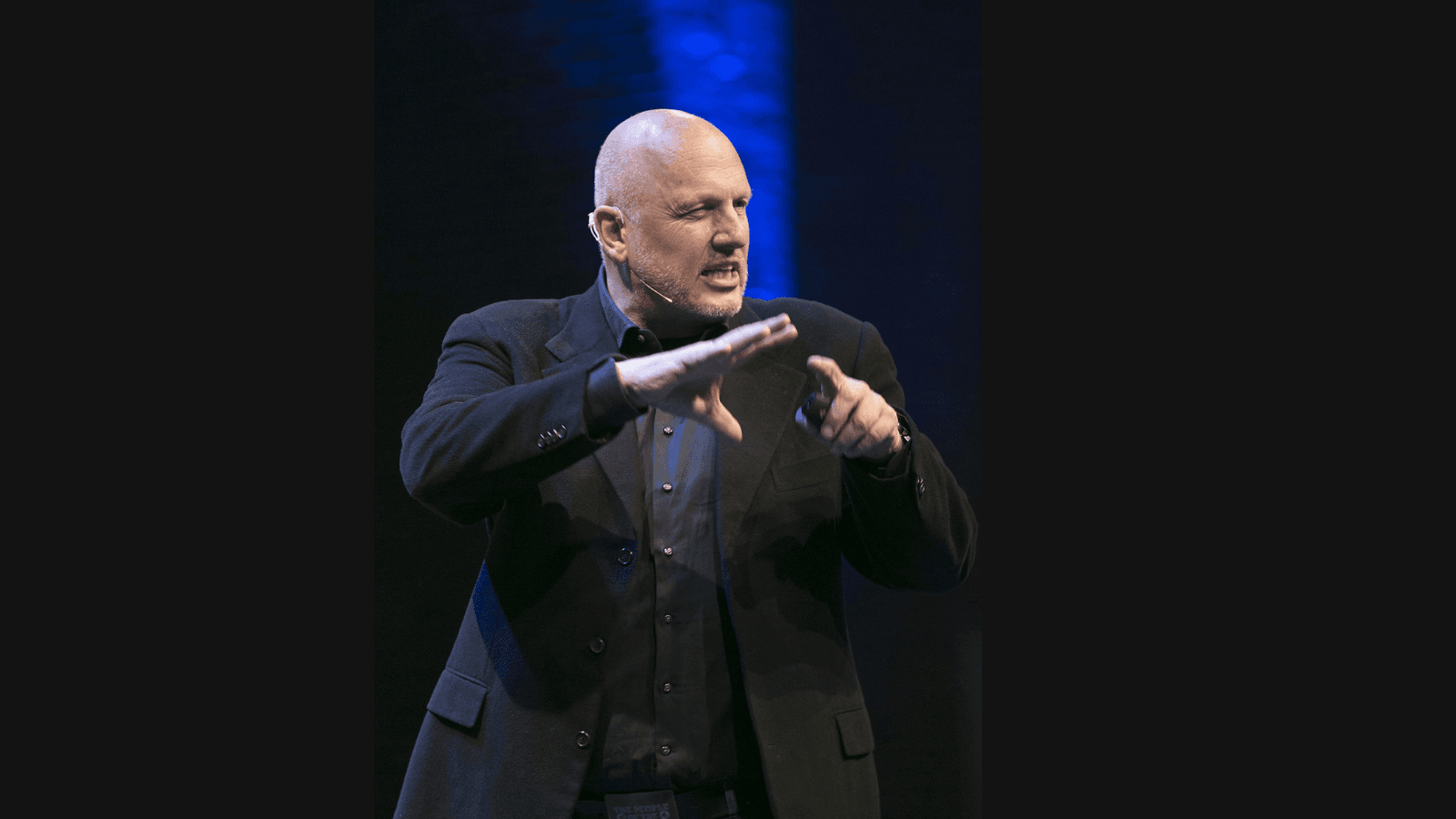 Ruud Veltenaar aan het spreken bewegend met handen in zwart pak