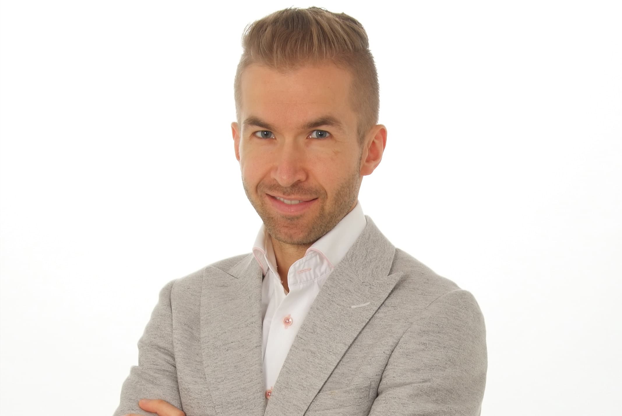 Richard Jansen glimlachend poserend met armen over elkaar heen in grijs pak bij witte achtergrond