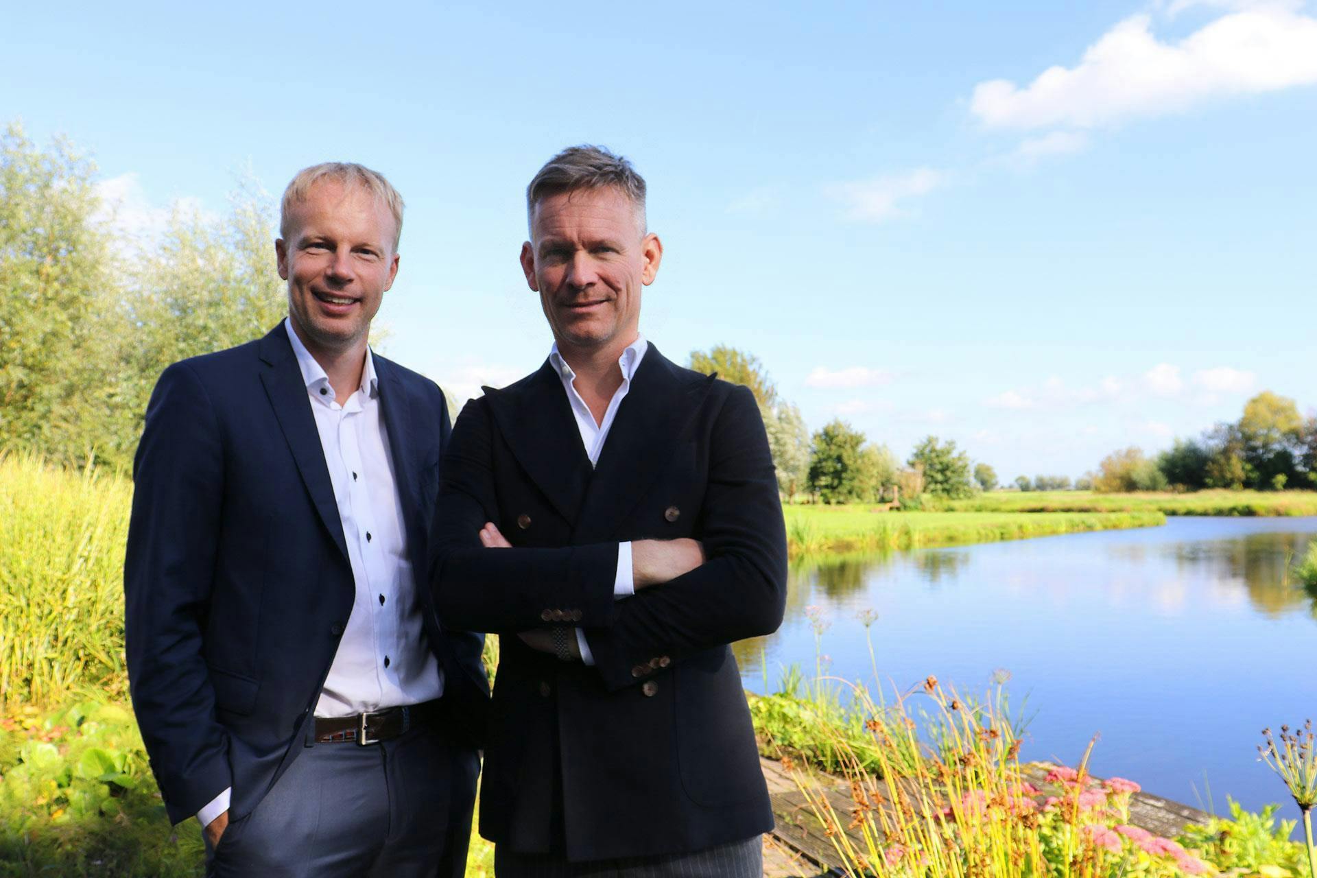 Arno Folkerts en Paul Smit poserend in pak glimlachend bij het meer 