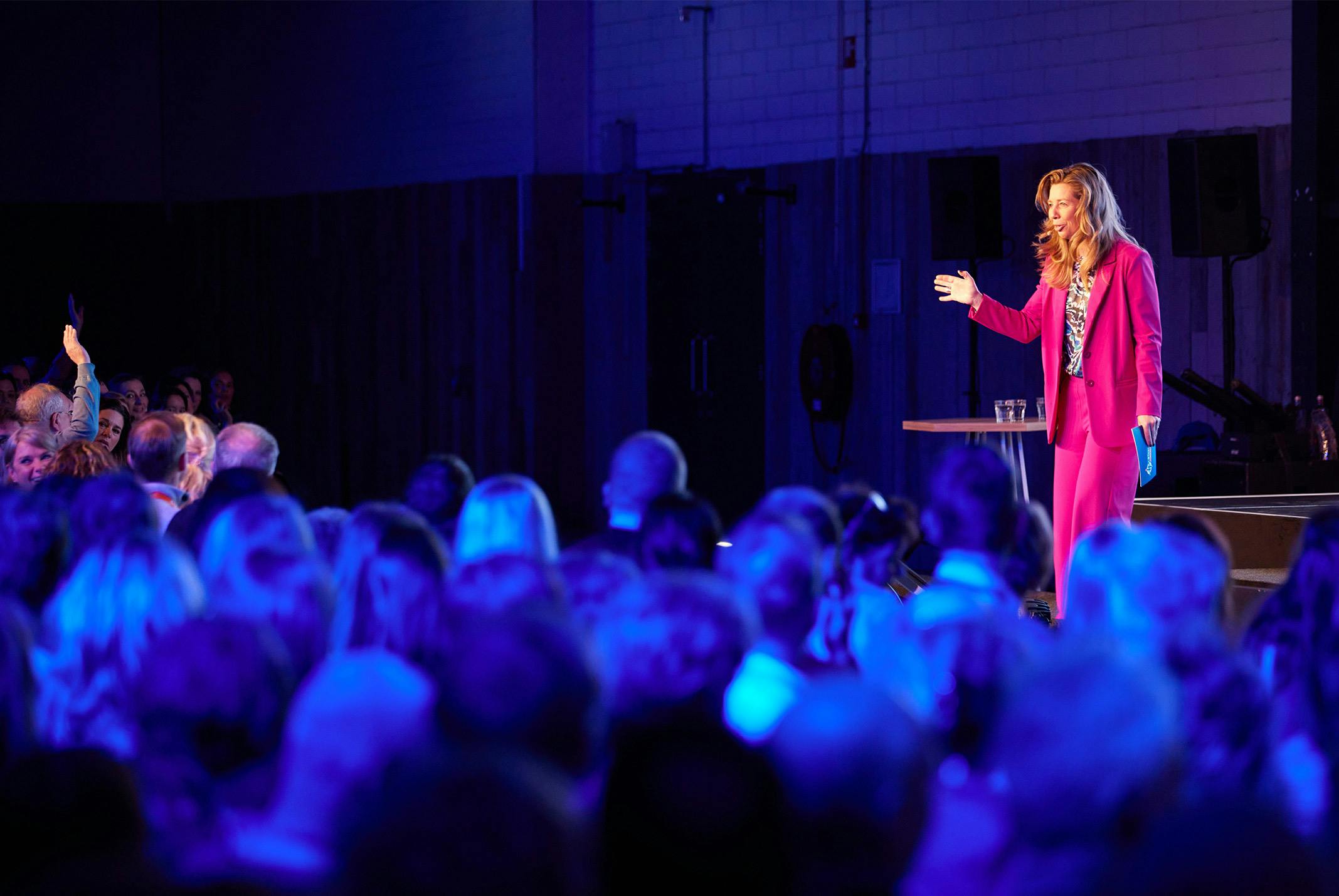 Pauline de Wilde op het podium in een roze pak tijdens een evenement sprekend naar het publiek