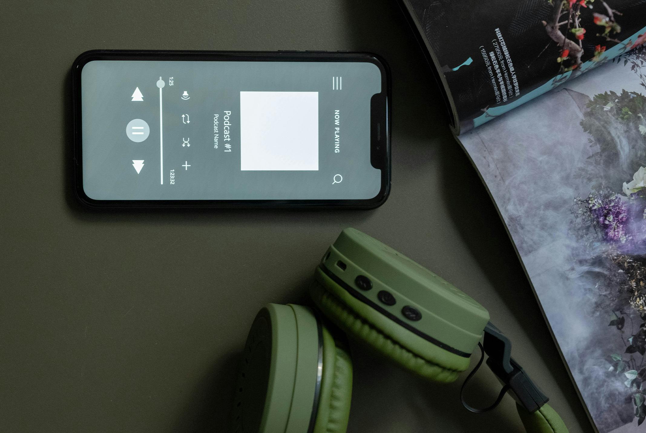 Een telefoon die aanstaat met een podcast app open en een mint-groene koptelefoon ernaast.