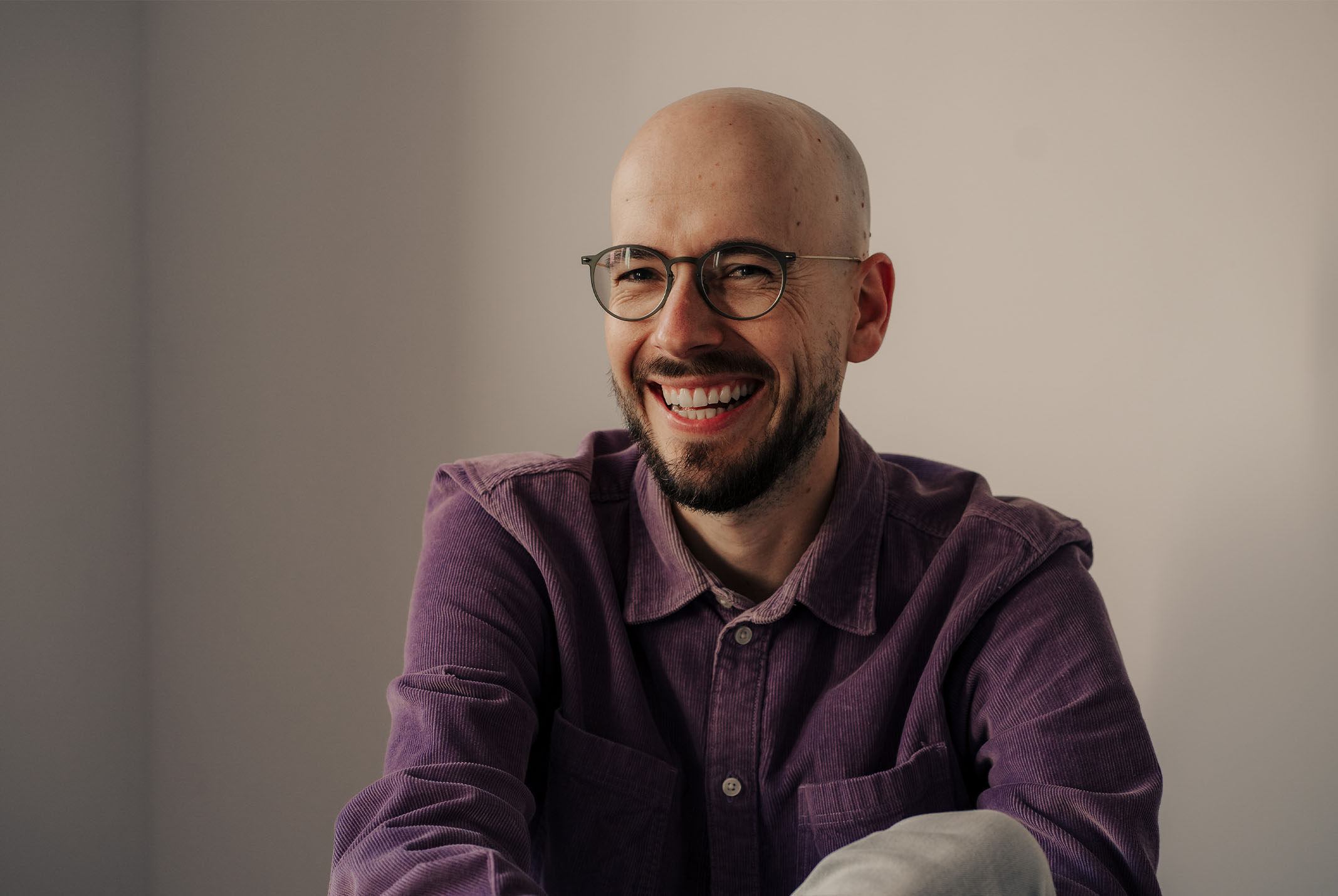 Man die lacht met bril achtere een beige achtergrond