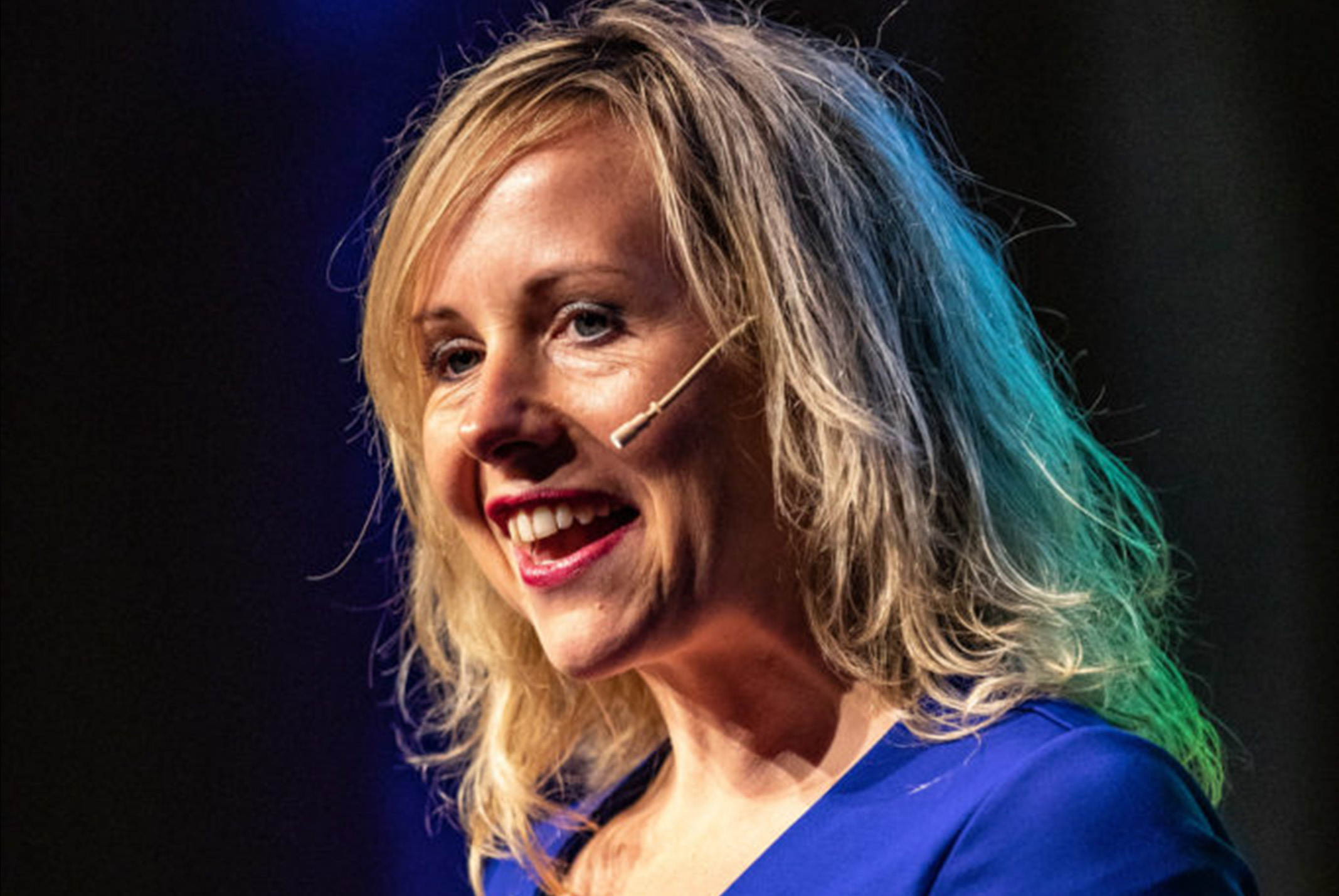 Wendelien Wouters aan het spreken in blauw shirt bij zwarte achtergrond