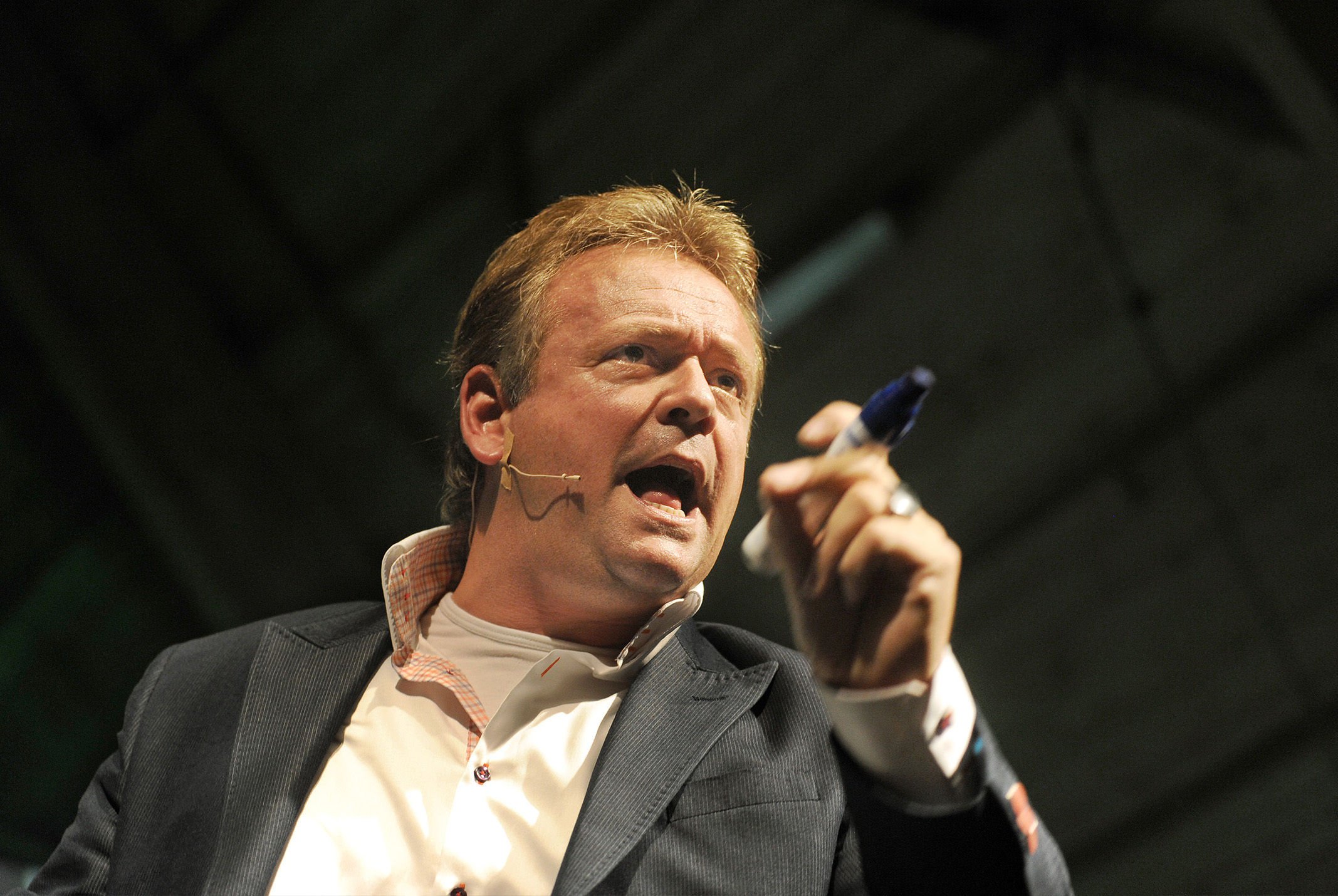 Jan van Setten met mond open in grijs pak met stift in hand