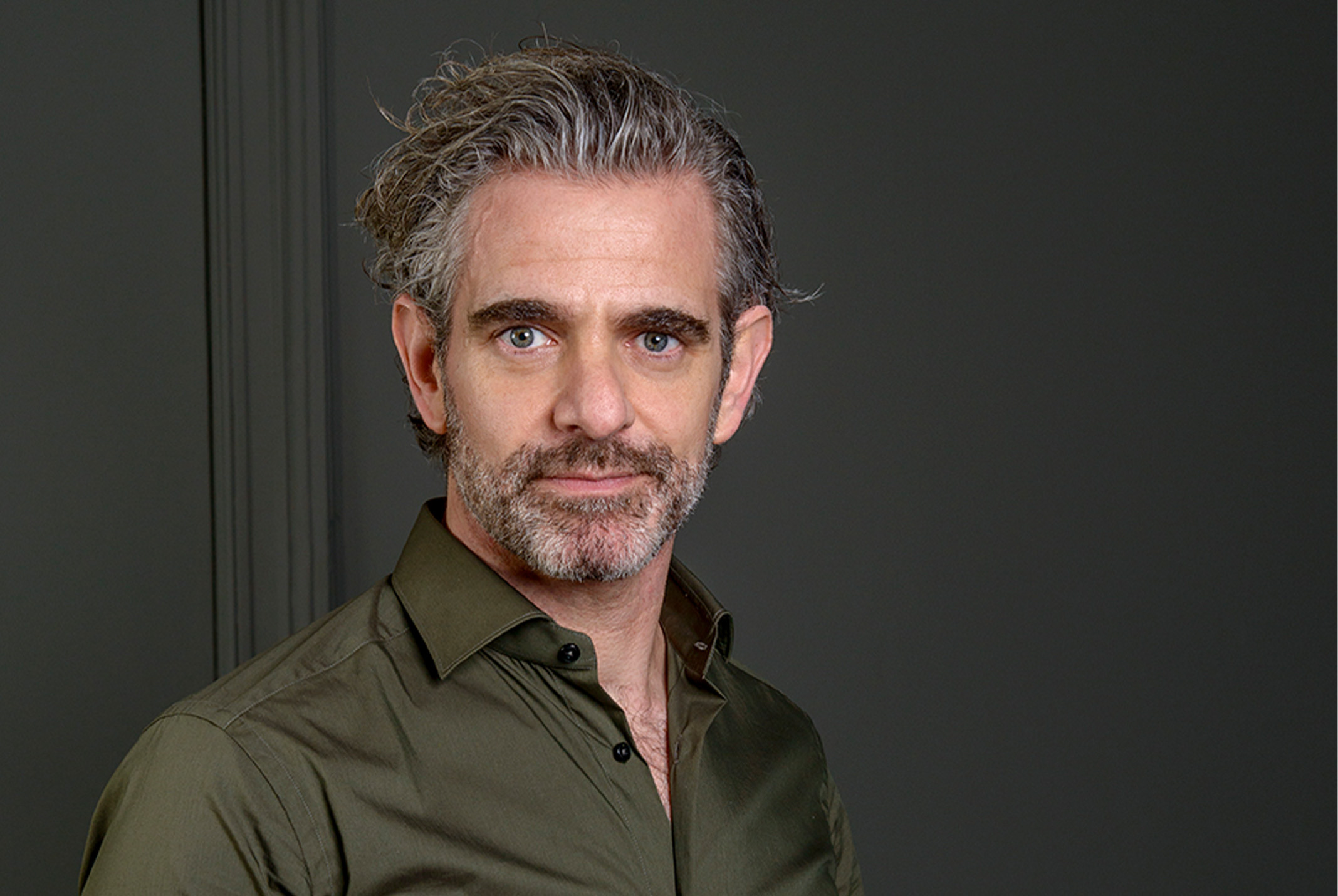 Raymond de Looze in groene overhemd voor grijze muur