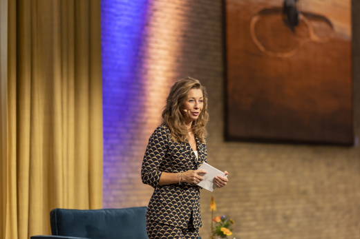 Pauline de Wilde in blazer op podium met geel gordijn