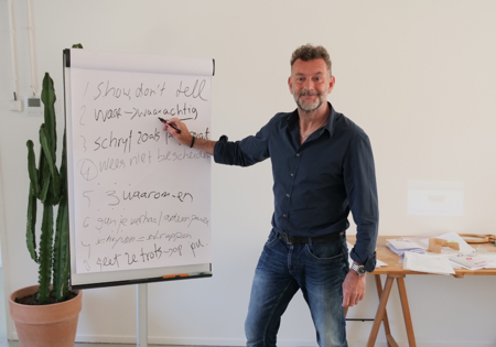 Raymond van de Klundert (Kluun) poserend met hand bij witte schrijfbord onderschreven