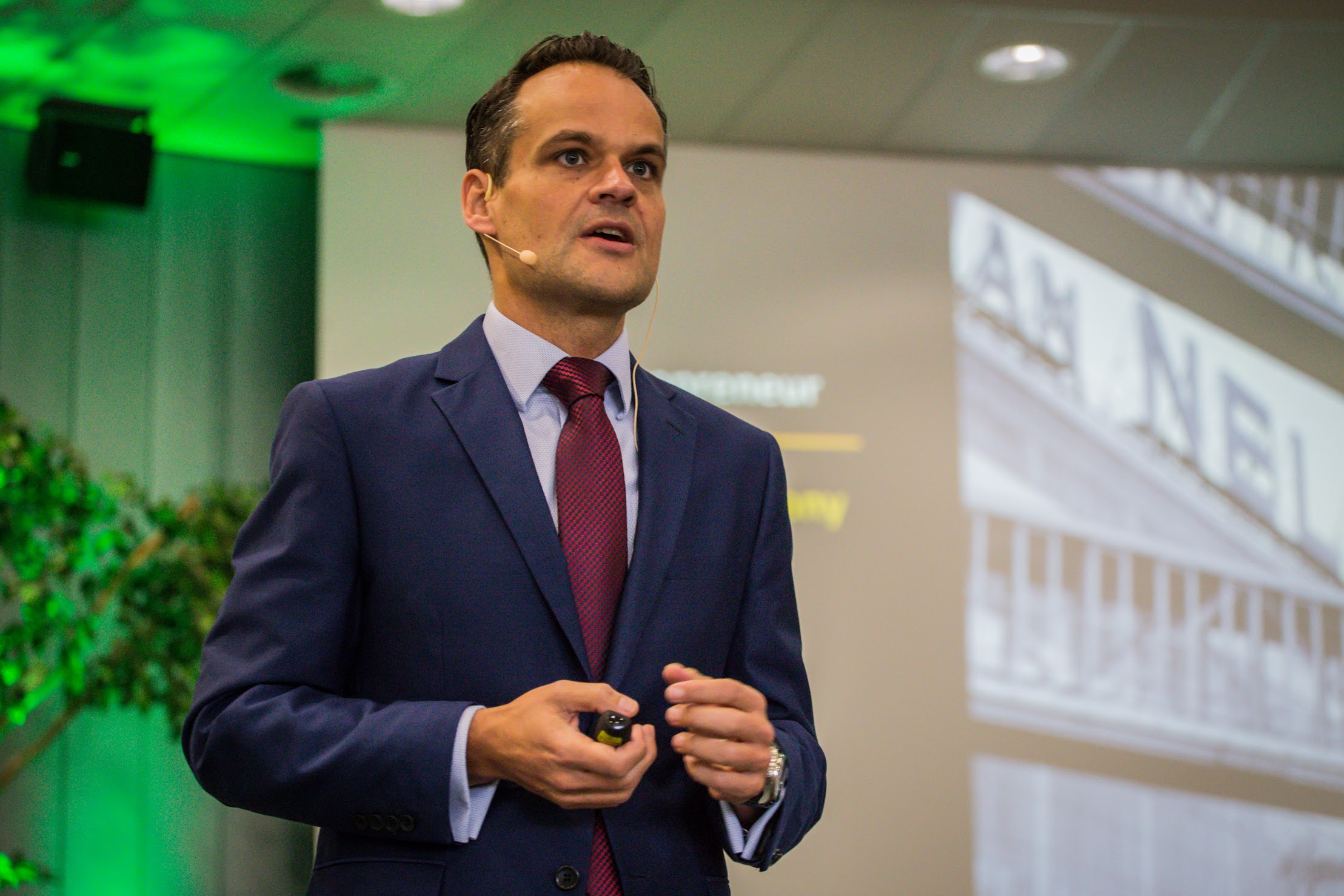 Jan Kees de Jager aan het presenteren in blauw pak met groen licht op achtergrond