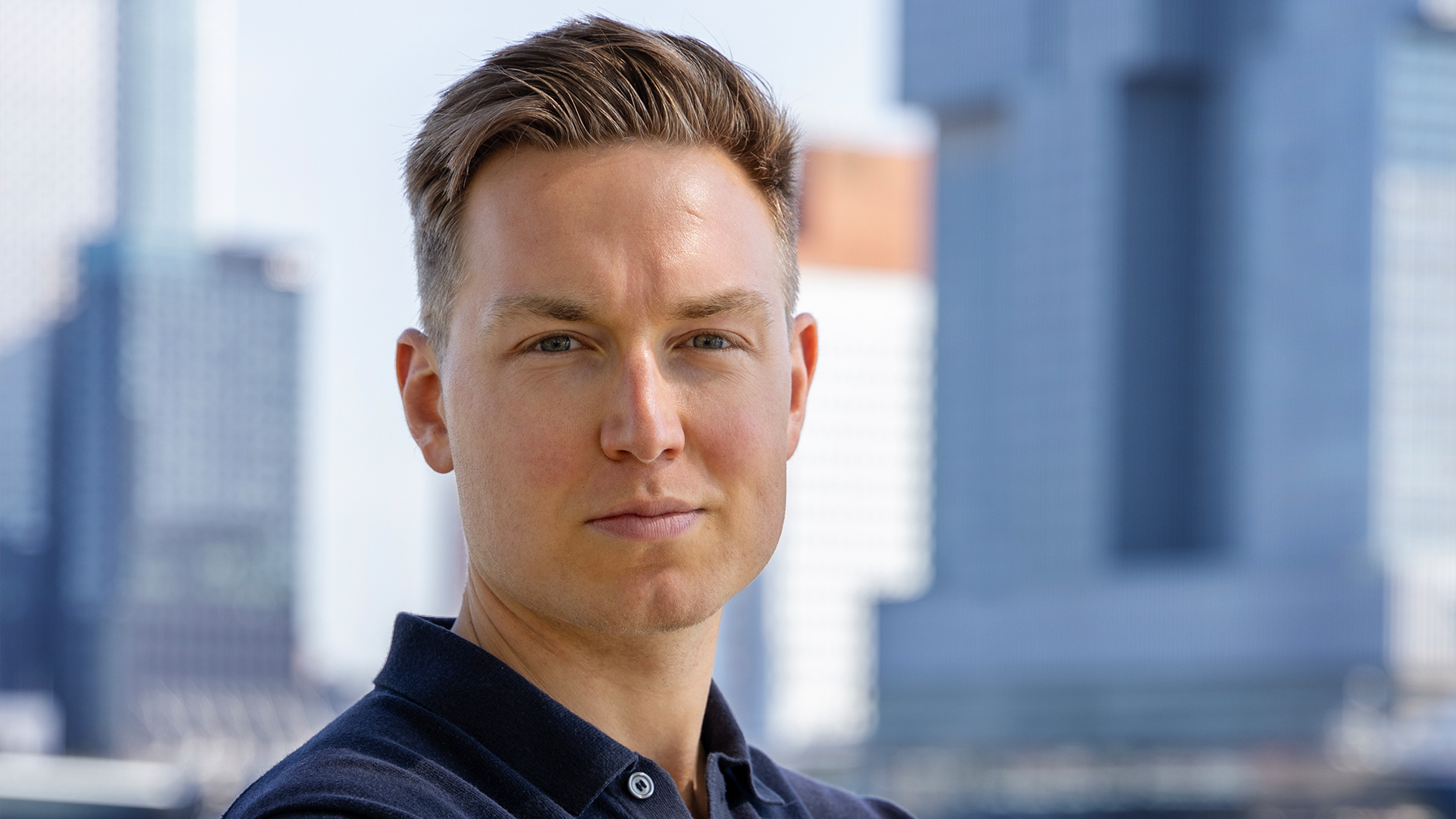 Man in een blauw shirt met armen over elkaar en is water op de achtergrond te zien