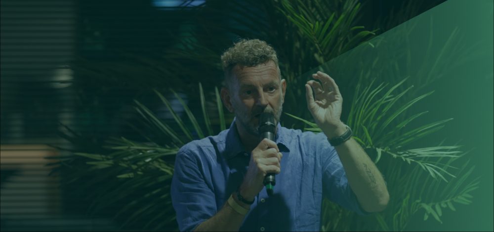 Kluun aan het spreken met een microfoon met een groene kleur erover heen en het Sprekershuys logo linksboven in