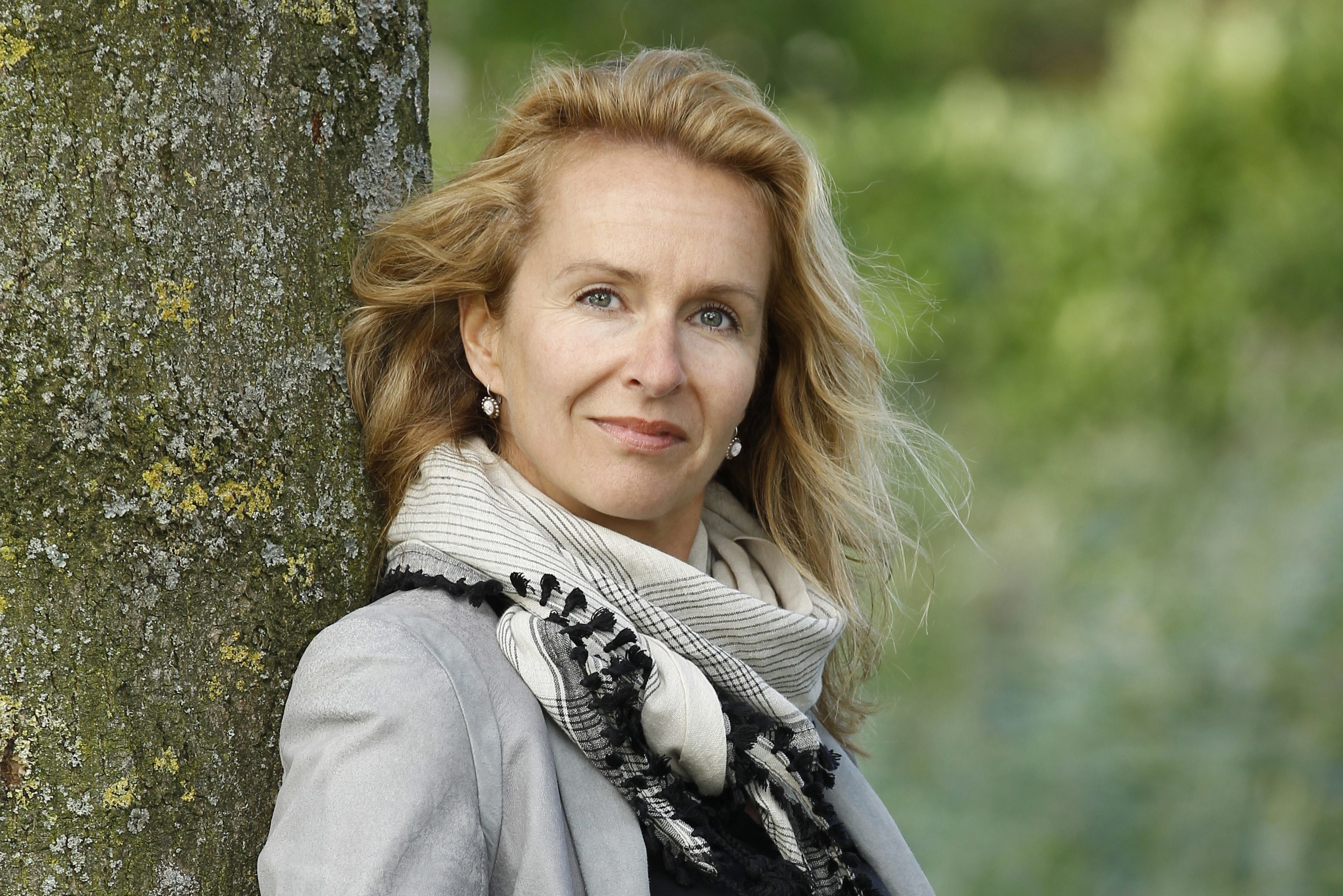 Pauline van Aken poserend in grijze blazer leunend tegen boom