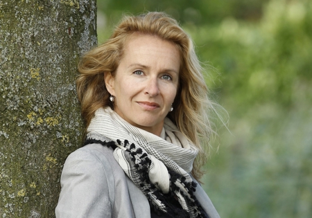 Pauline van Aken poserend in grijze blazer leunend tegen boom