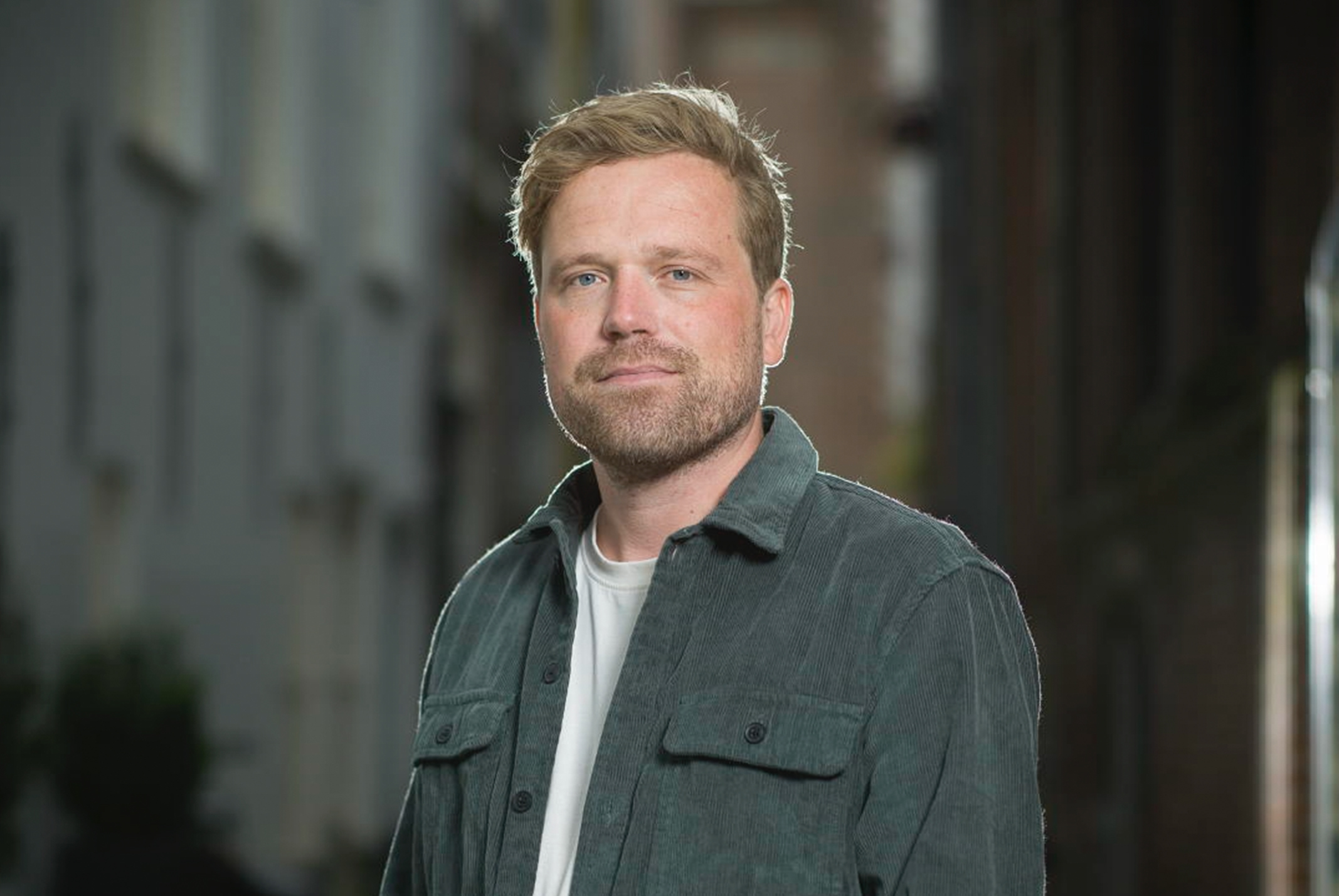 Man met een groen jasje aan met een donkere achtergrond