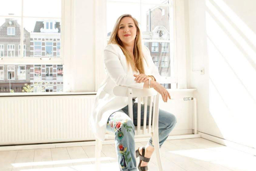 Dorit Roest in witte blazer op een witte stoel in witte ruimte