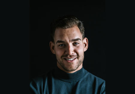 Mark Schadenberg glimlachend in zwarte koltrui bij zwarte achtergrond