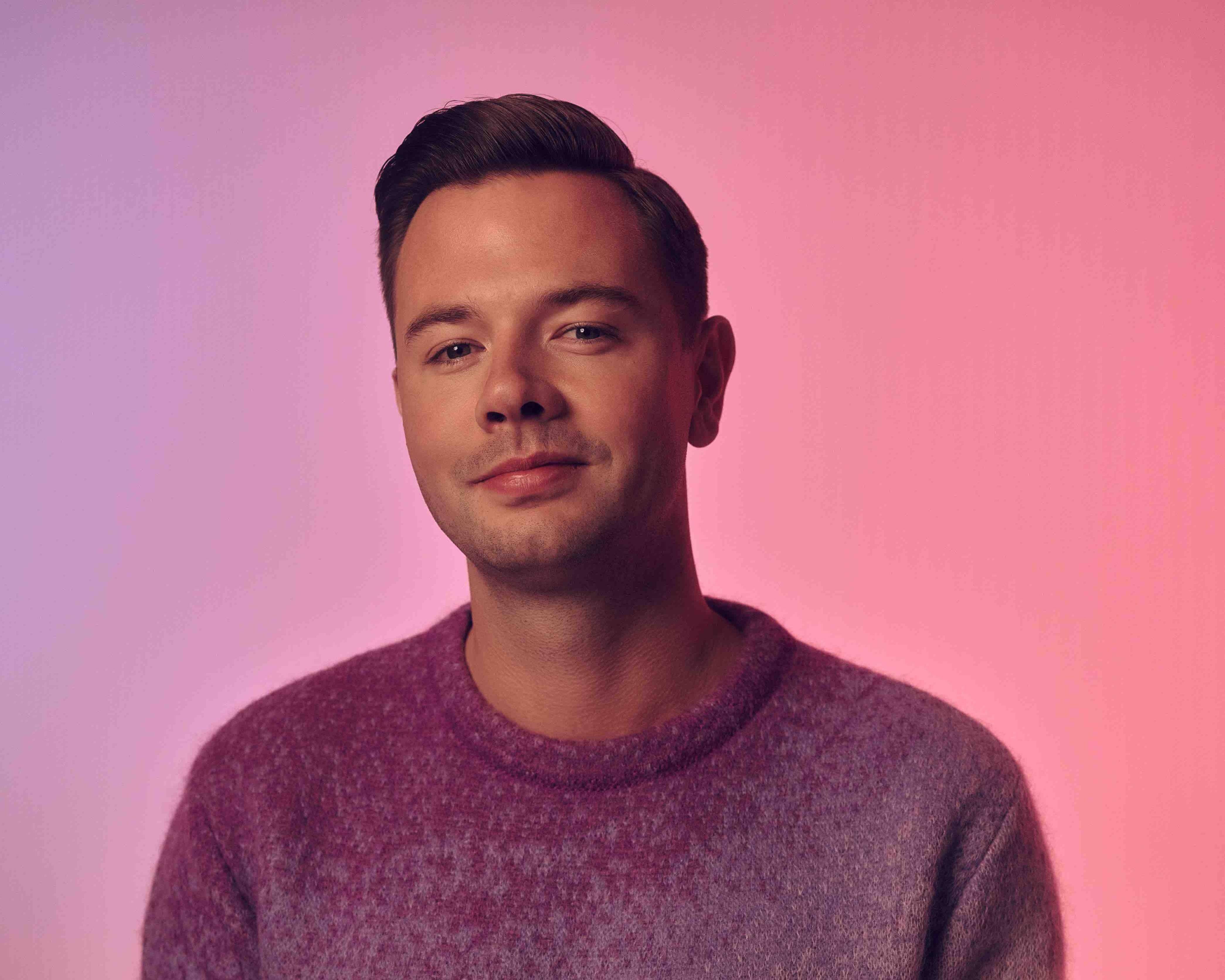 Sam Feldt poserend in roze en paarse sweater bij roze achtergrond