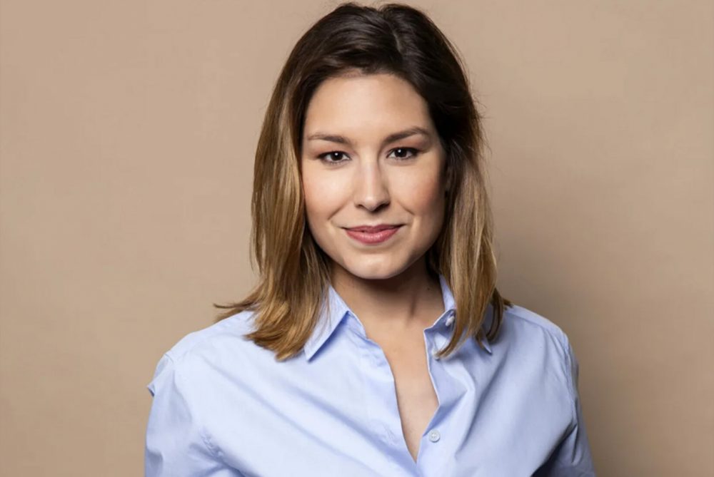 Amber Brantsen in blauwe blouse voor beige muur