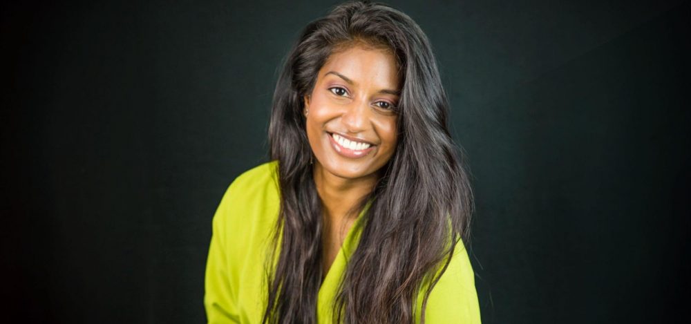 Gina Doekhie glimlachend in geel shirt bij zwarte achtergrond