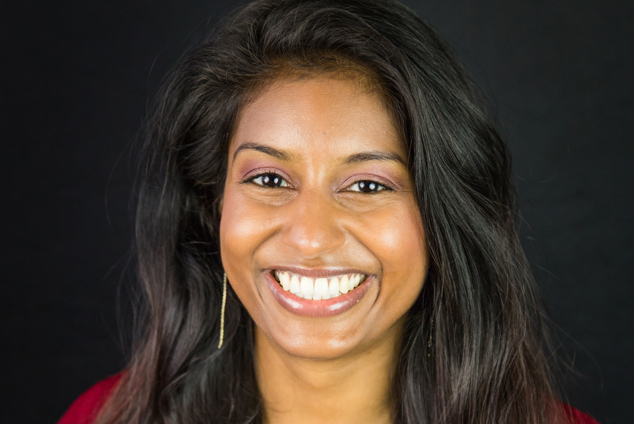 Gina Doekhi glimlachend in rood shirt bij zwarte achtergrond