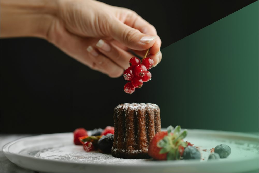 Hand met rode bessen op een chocolade dessert