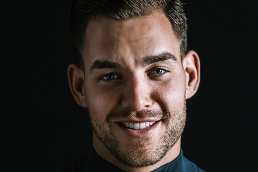 Mark Schadenberg glimlachend in zwarte koltrui bij zwarte achtergrond