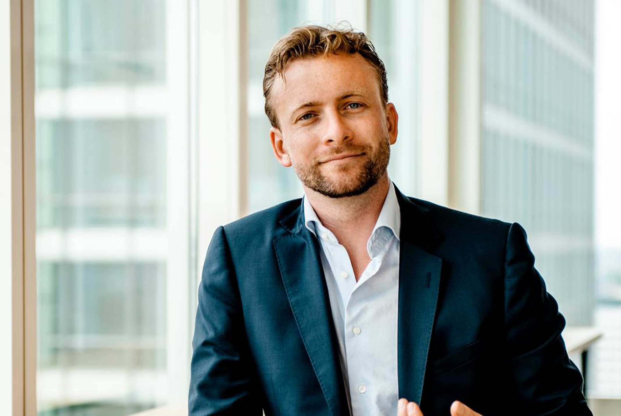 Thijs Launspach glimlachend in blauw pak bij ramen