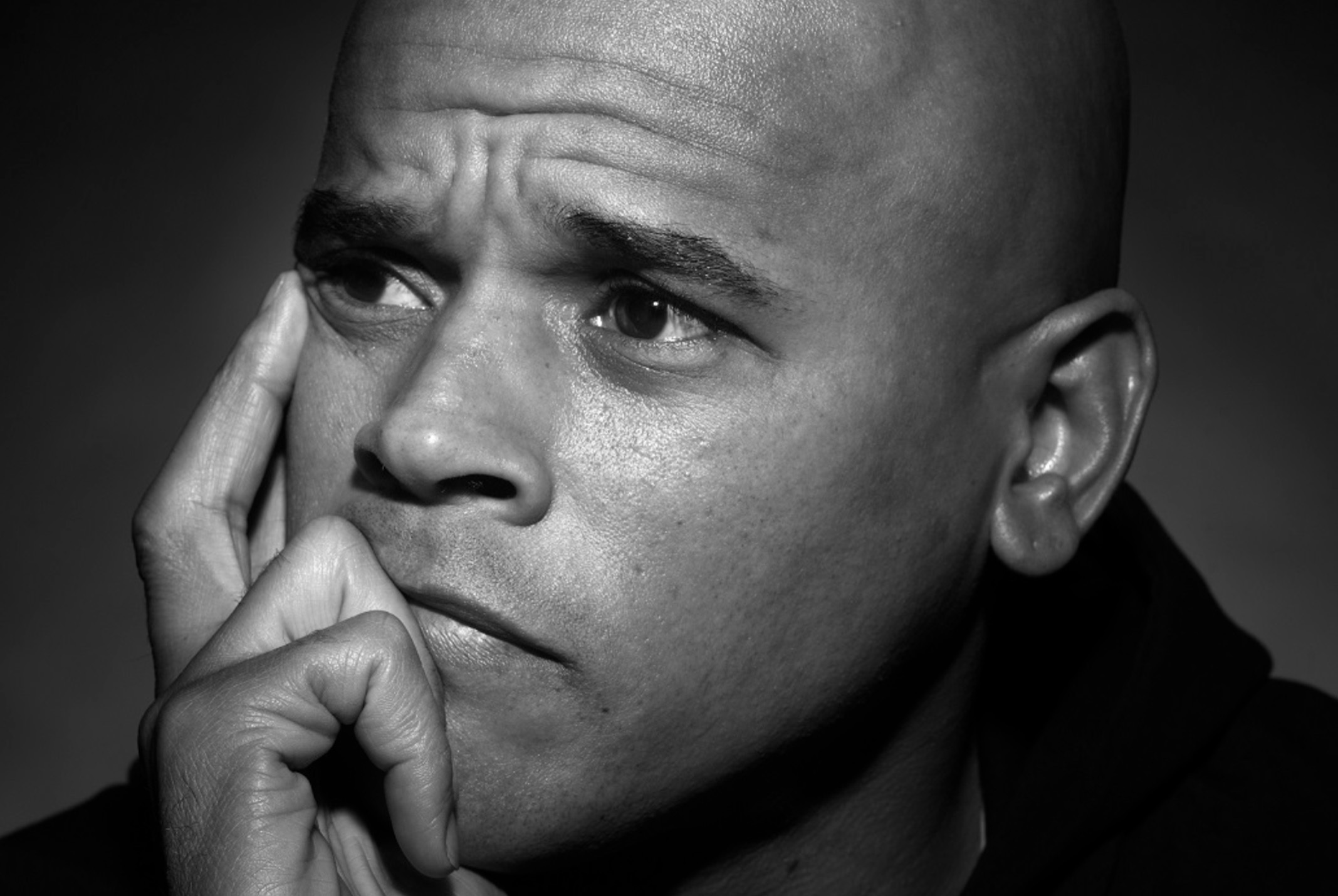 Zwart-wit foto van Glenn. Hij kijkt droevig en heeft een hand bij zijn gezicht. Hij kijkt niet in de camera