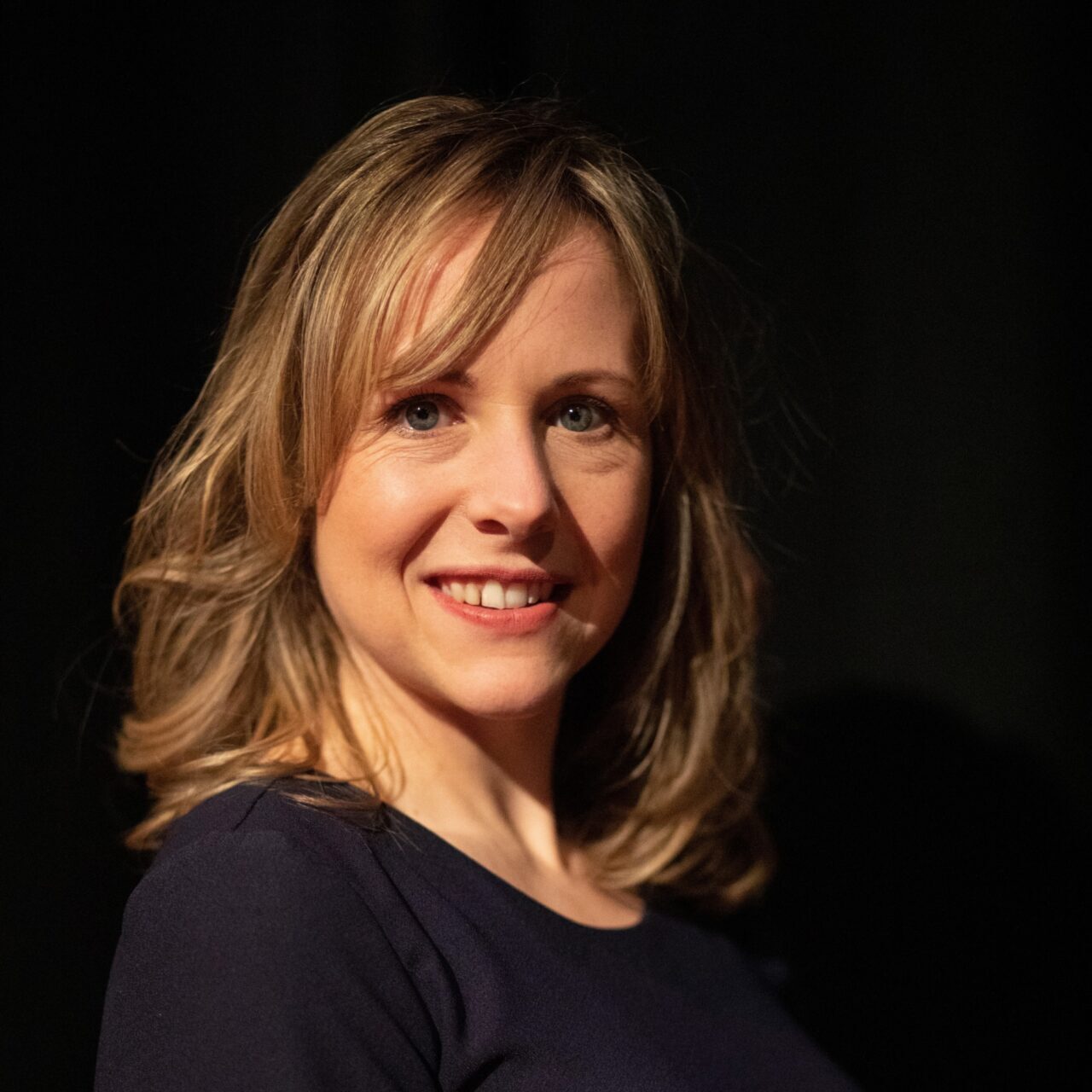 Wendelien Wouters glimlachend in zwart shirt bij zwarte achtergrond