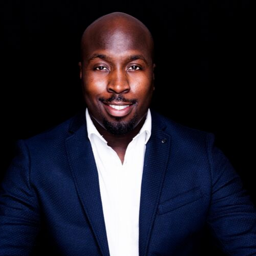 Fernando Halman poserend lachend in blauw pak bij zwarte achtergrond