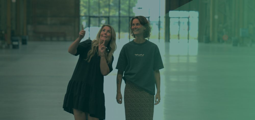 Claire Clement en Vivian Goudkuil glimlachend kijkend naar boven met groene gloed over zich