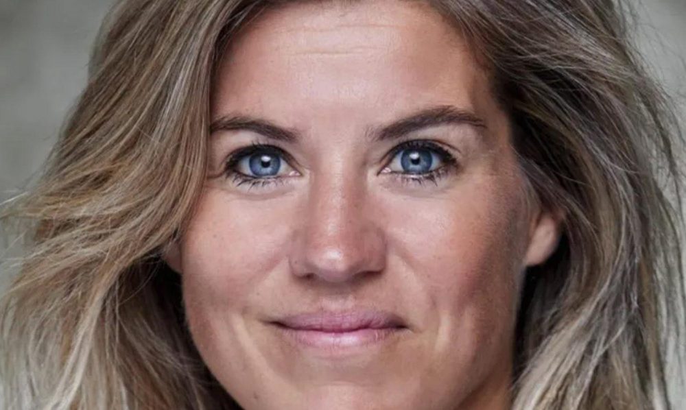 Kim Lammers lachend met mond dicht bij grijze achtergrond