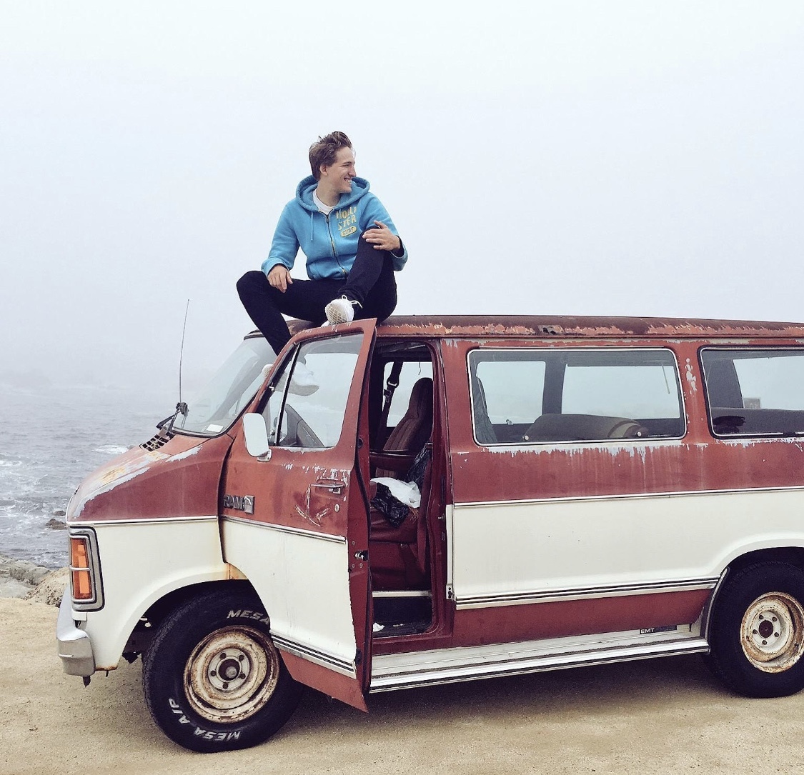 Bas Tietema in blauwe hoodie zittend op een rood met wit busje kijkend naar zijkant