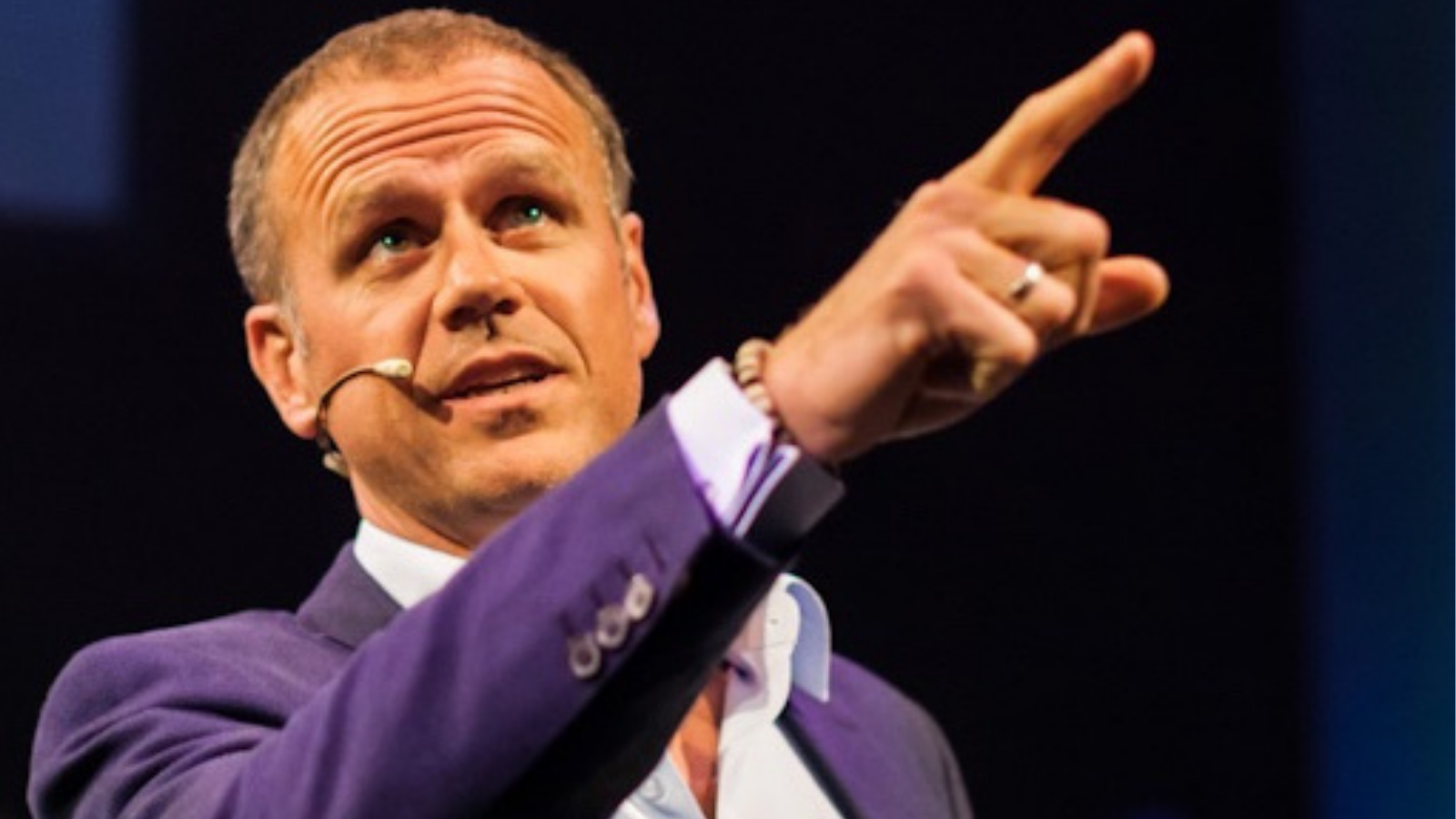 Ynzo van Zanten presenteert in pak en wijst met vinger