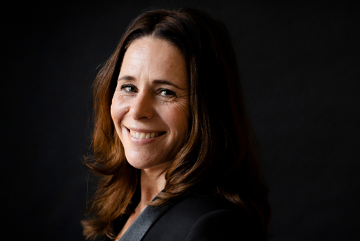 Irma Sluis glimlachend met zwarte blazer bij zwarte achtergrond