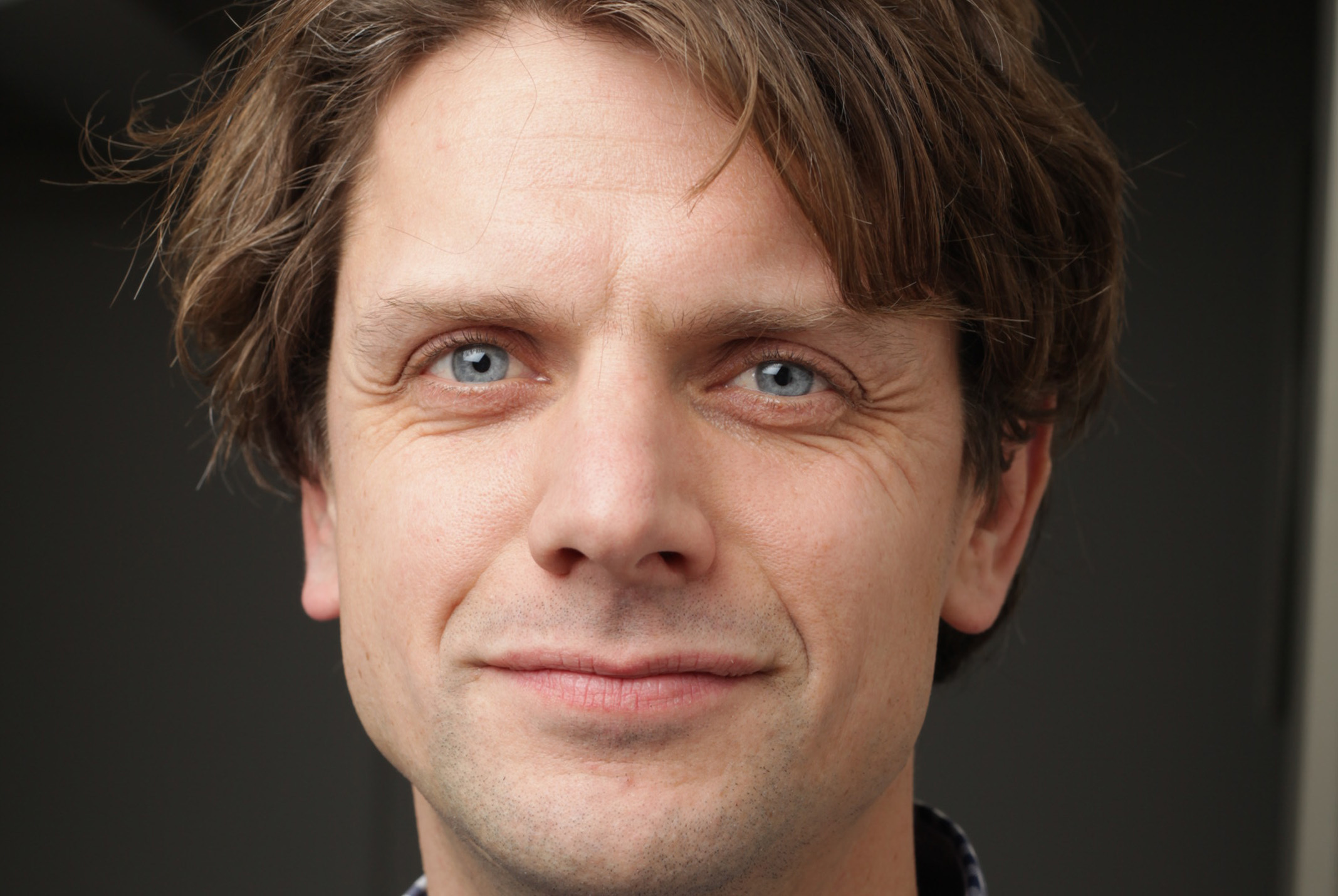 Jaap Vriend poserend in wit en blauwe geruiten blouse bij grijze achtergrond