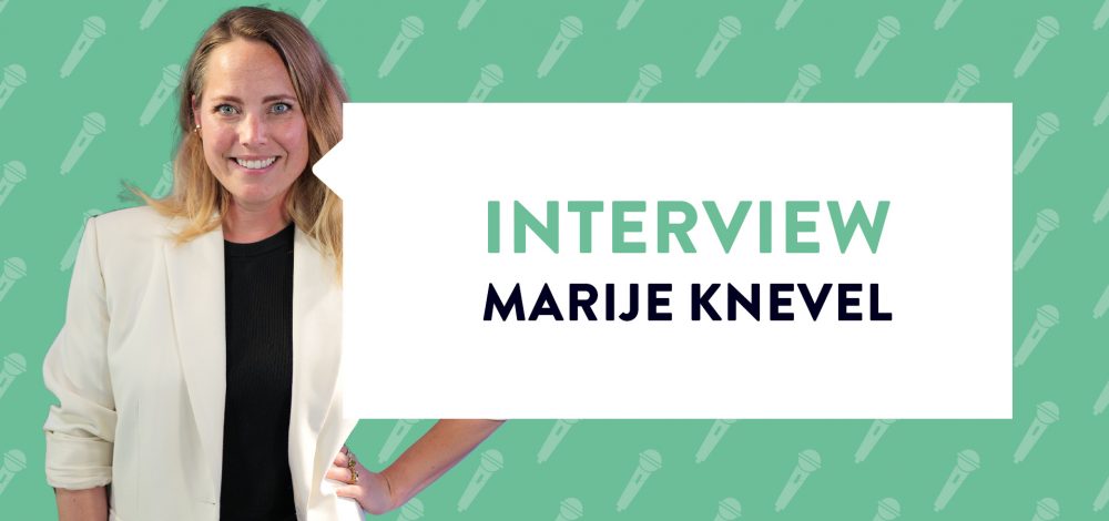 Marije Knevel glimlachend in witte blazer met groene achtergrond