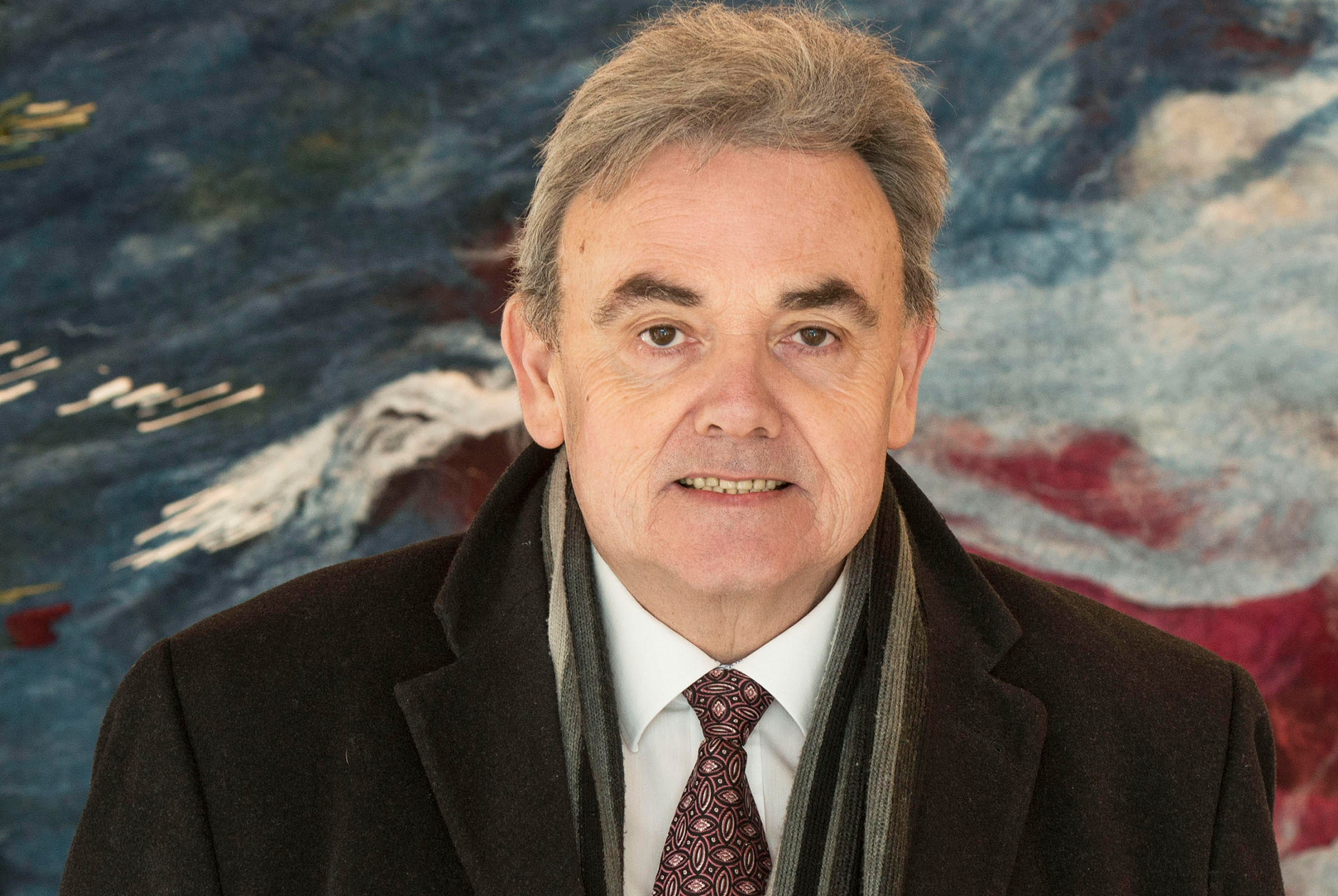 Willem Post poserend in zwarte jas en grijze sjaal bij kleurrijke achtergrond