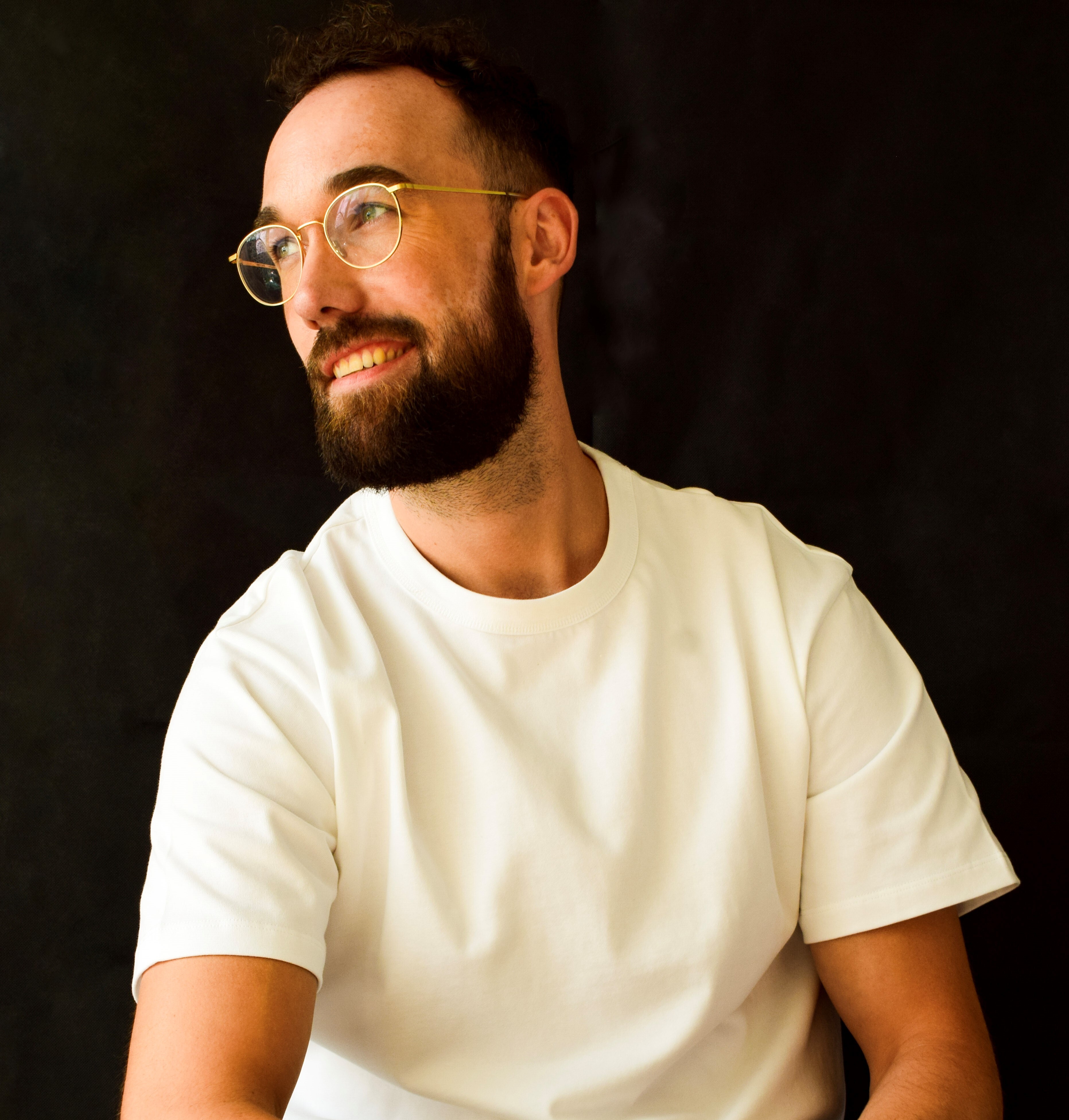 Rudy van Belkom kijkt naar links lachend met wit shirt en zwarte achtergrond