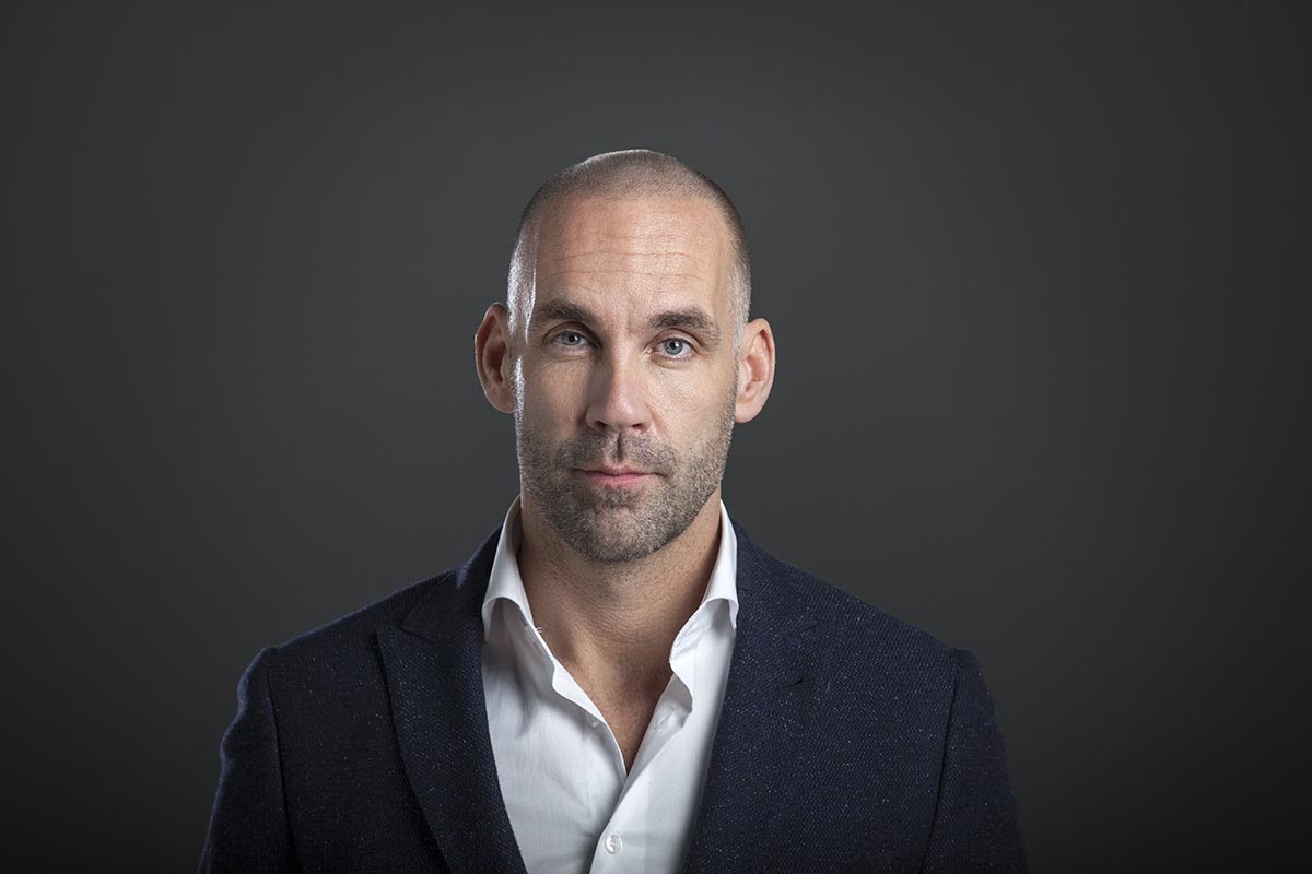 Richard van Hooijdonk poserend in pak bij grijze achtergrond