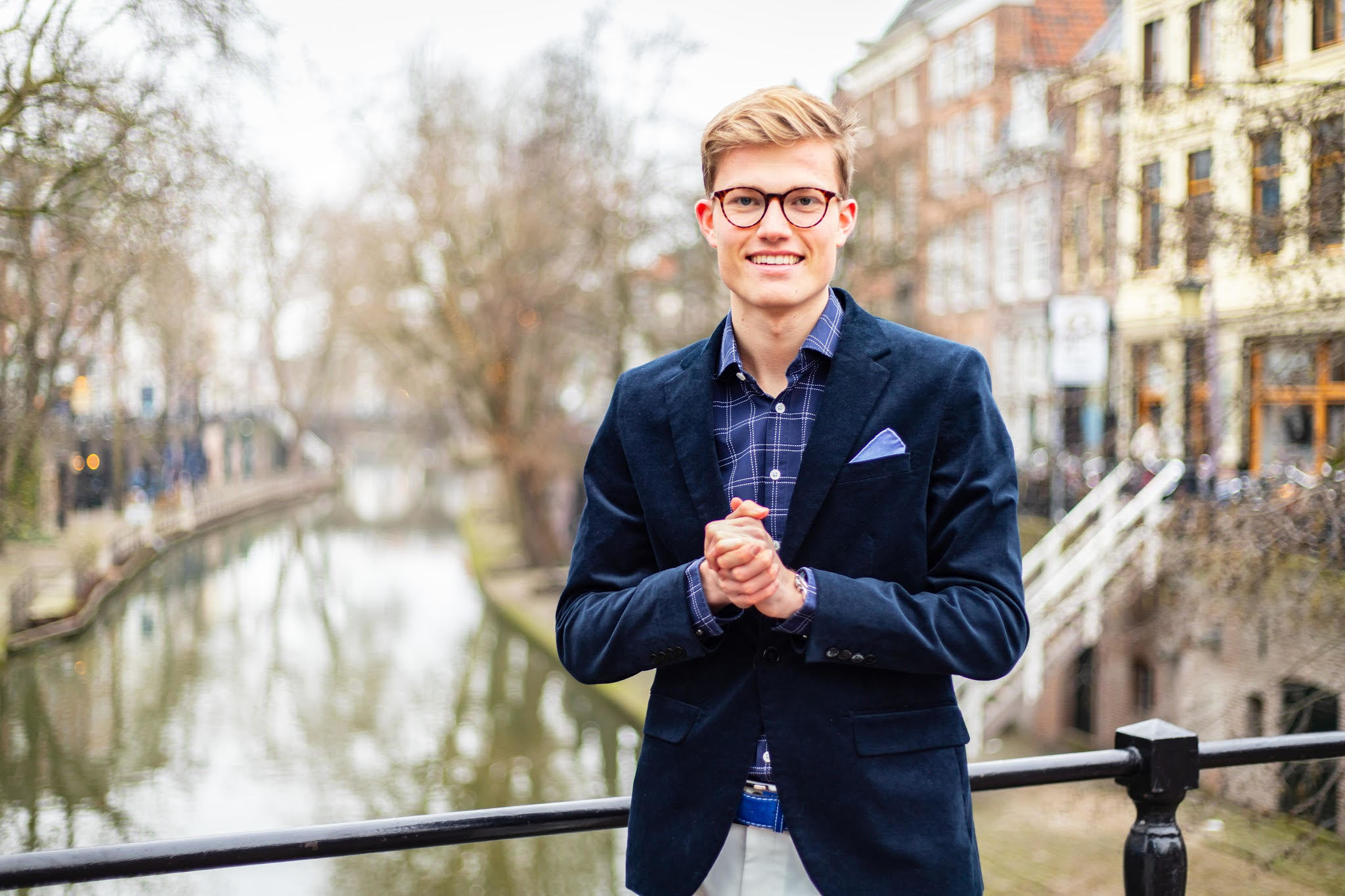 Jort Verhage lachend in blauw pak buiten bij grachten met handen bij elkaar