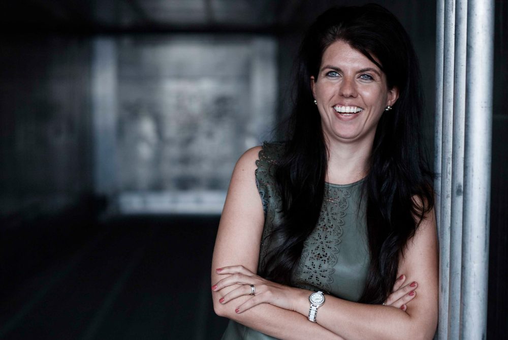 Kristel Groenenboom aan het lachen leunend tegen grijze muur