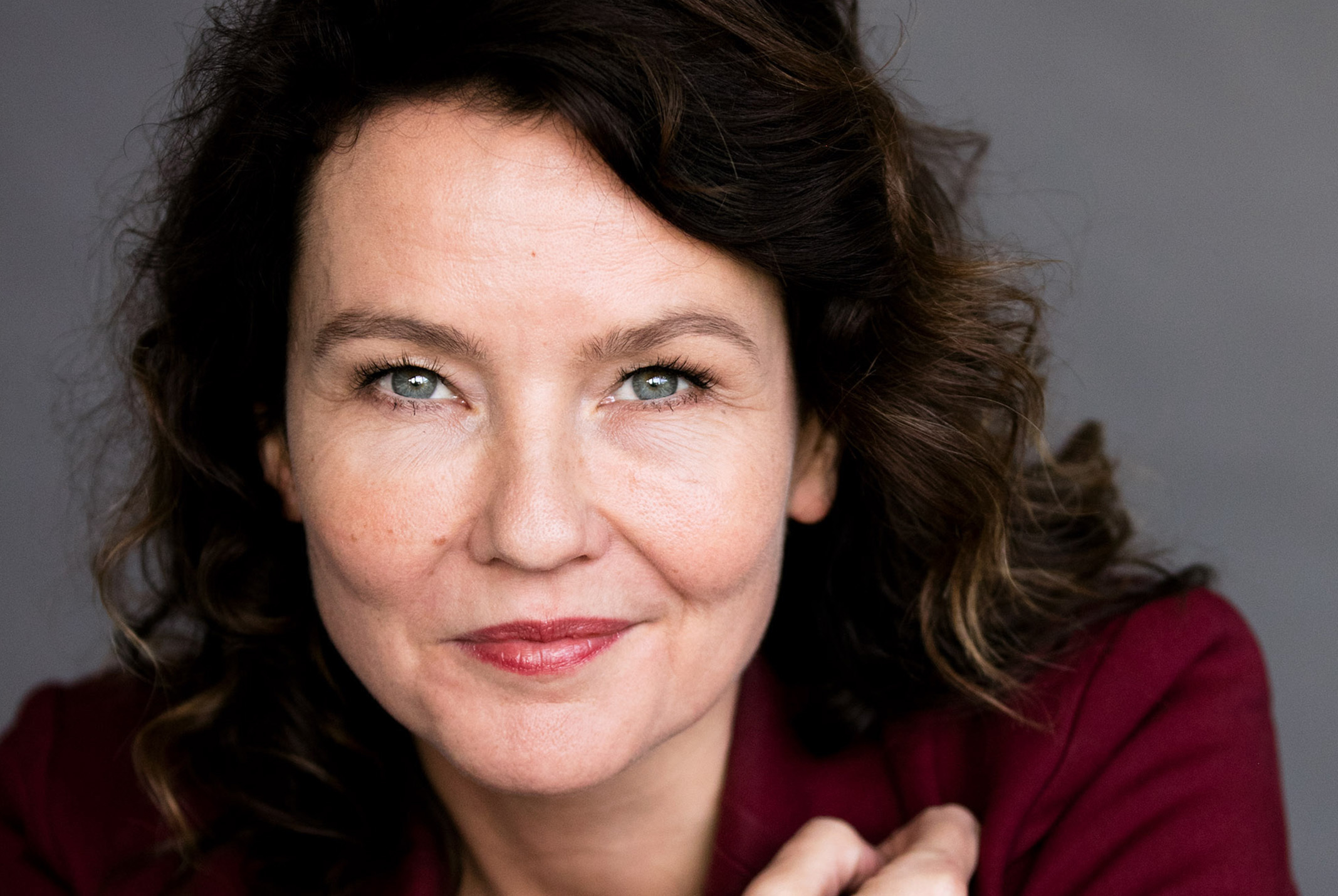 Kim Coppes poserend met rode blouse en grijze achtergrond