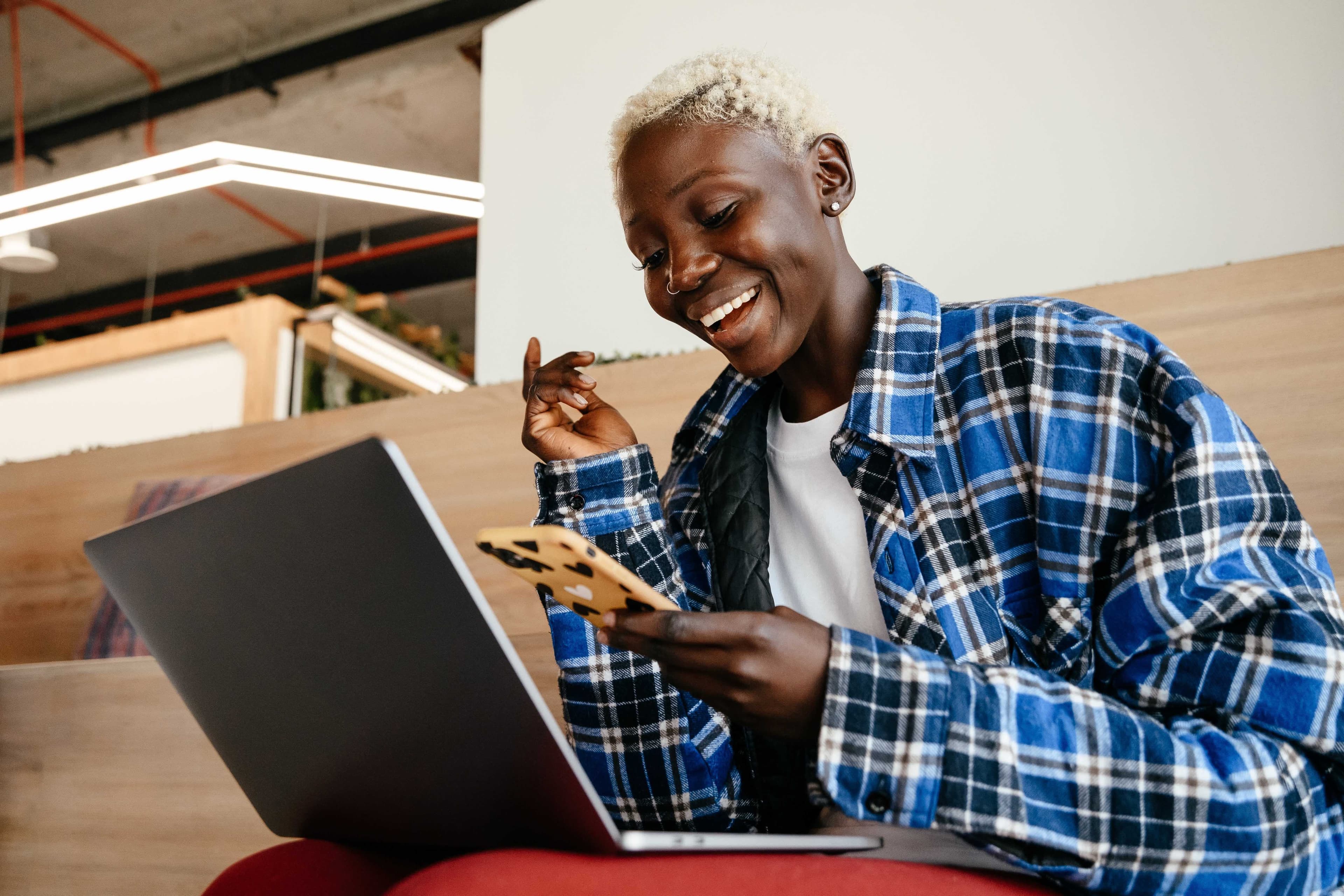 Vrouw glimlachend naar telefoon en laptop